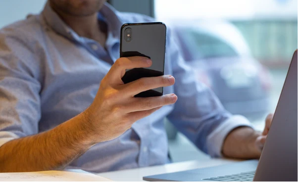 Mężczyzna korzystający ze smartfona podczas pracy przy laptopi